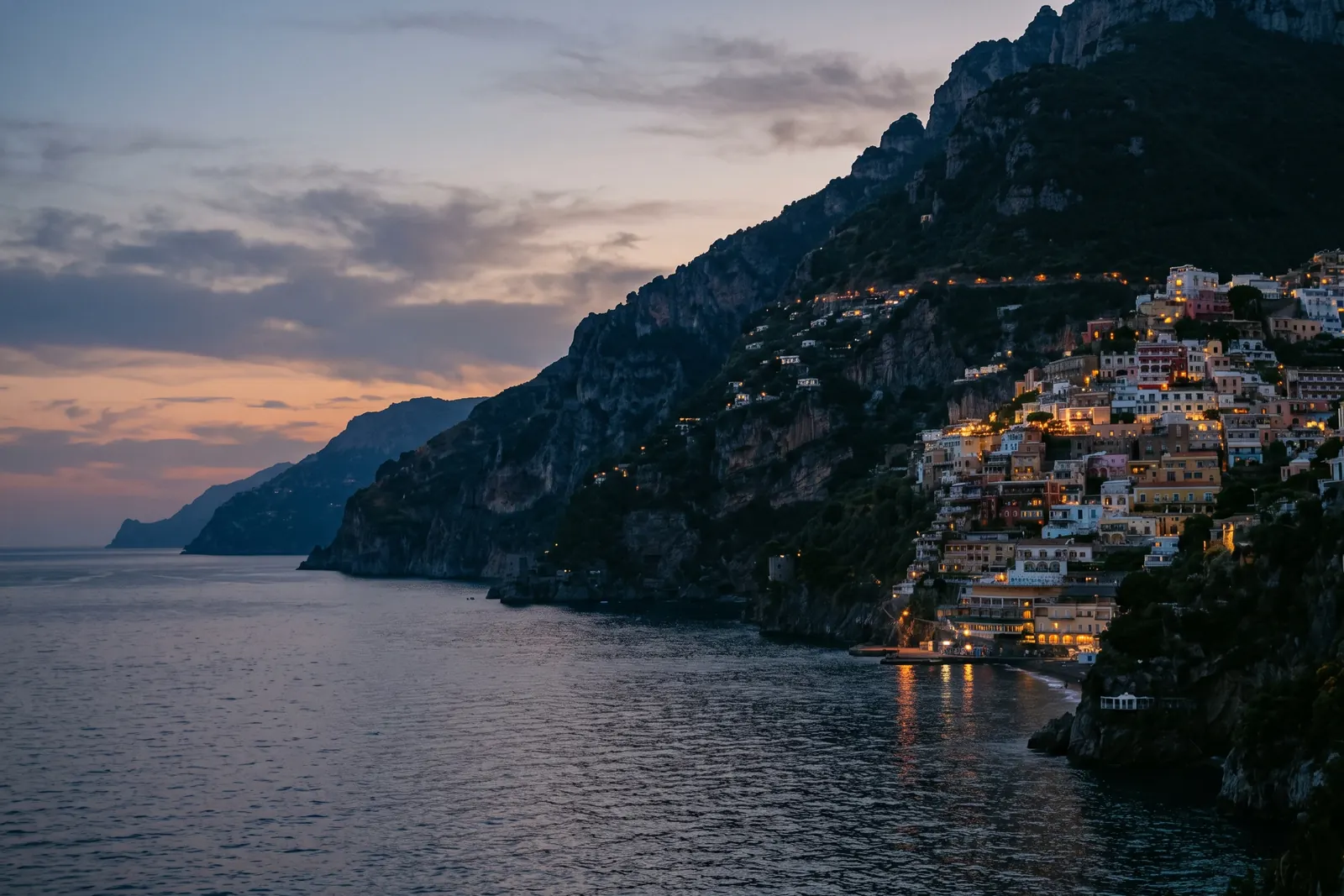 Amalfi Coast cliffs at dusk, pastel villages above a calm sea