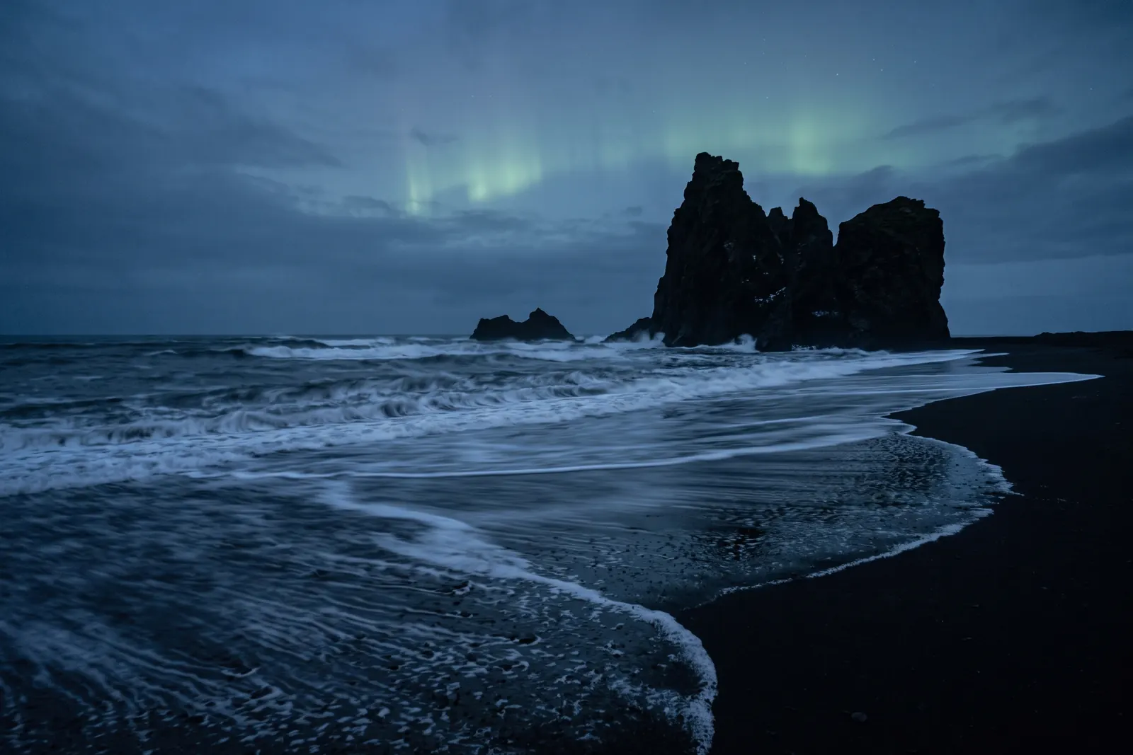Icelandic black sand coast at dusk beneath a pale green aurora