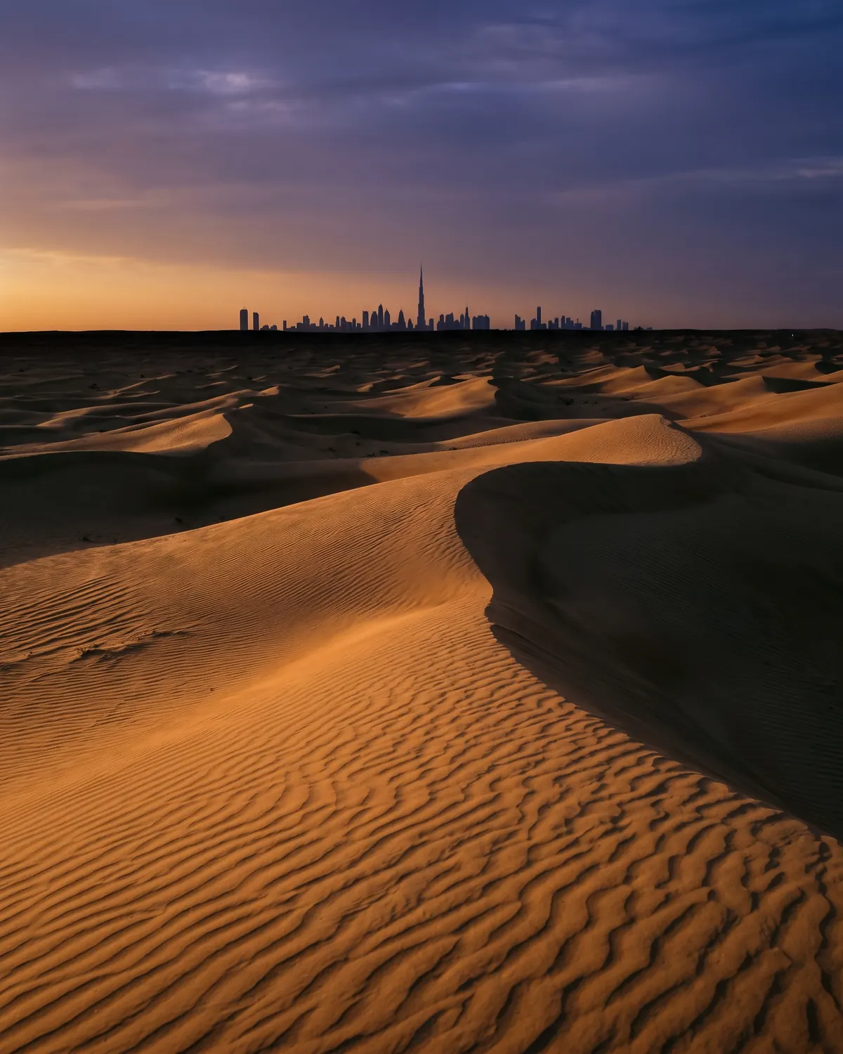 Dubai desert at dusk, dunes rolling towards the distant city skyline